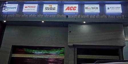 A lit strip of brand panels at Jay Shree Infra at night: sanitaryware, Prince, UltraTech, ACC, Nuvoco and MP Birla Cement, over a Hindi line and the shutters below