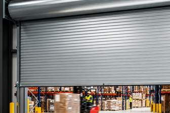A steel rolling shutter partly raised over a warehouse doorway, of the kind we supply