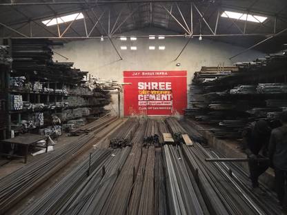 Rows of TMT sariya on the shed floor at Jay Shree Infra, racked sections either side, a Shree Cement board on the back wall