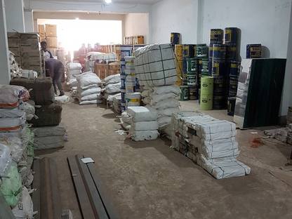 The store room at Jay Shree Infra, wrapped bundles tied with cord, stacked sacks, and pails and cartons along the wall